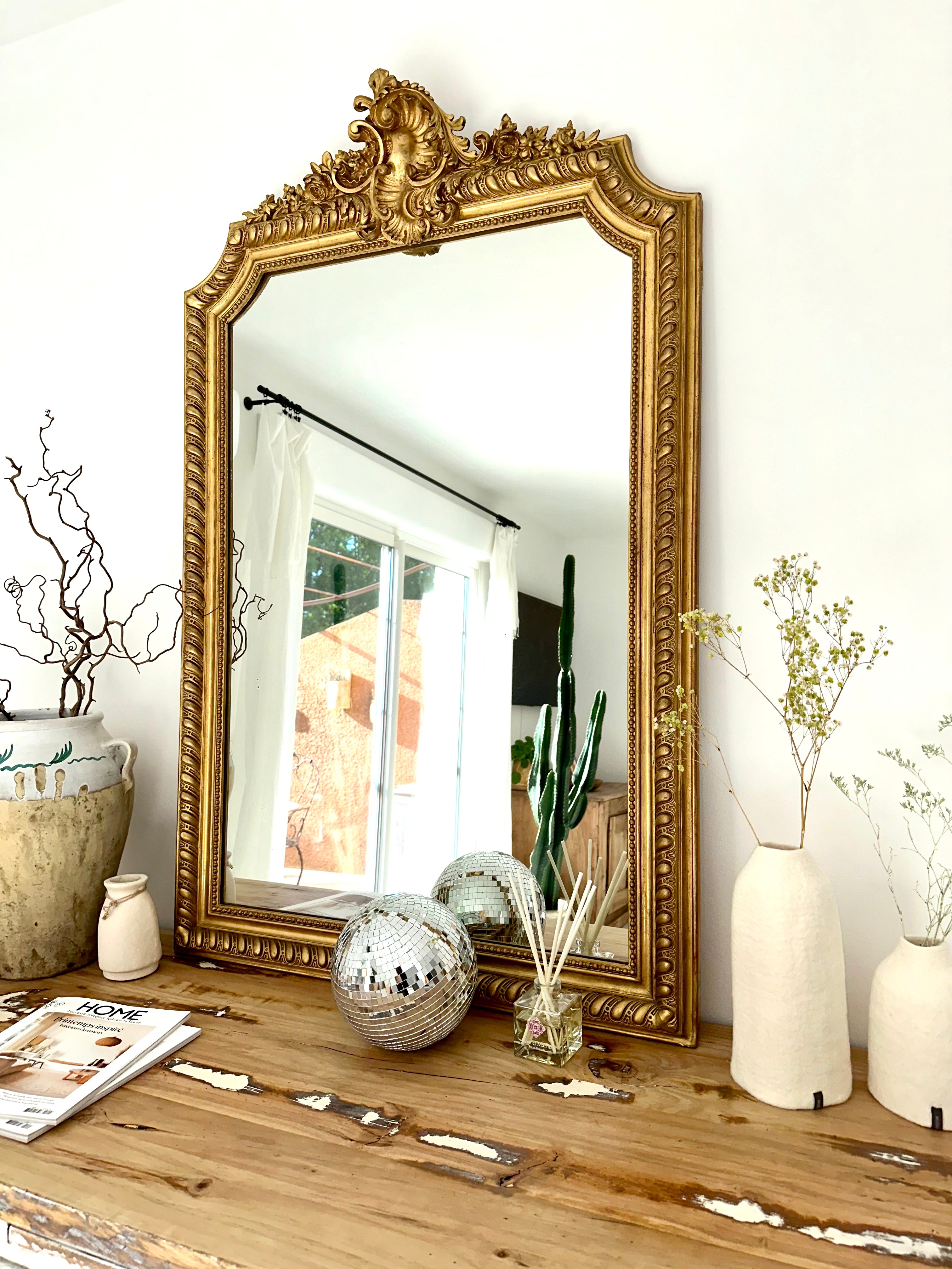 Un miroir ancien doré posé sur un buffet avec des vases et fleurs séchées