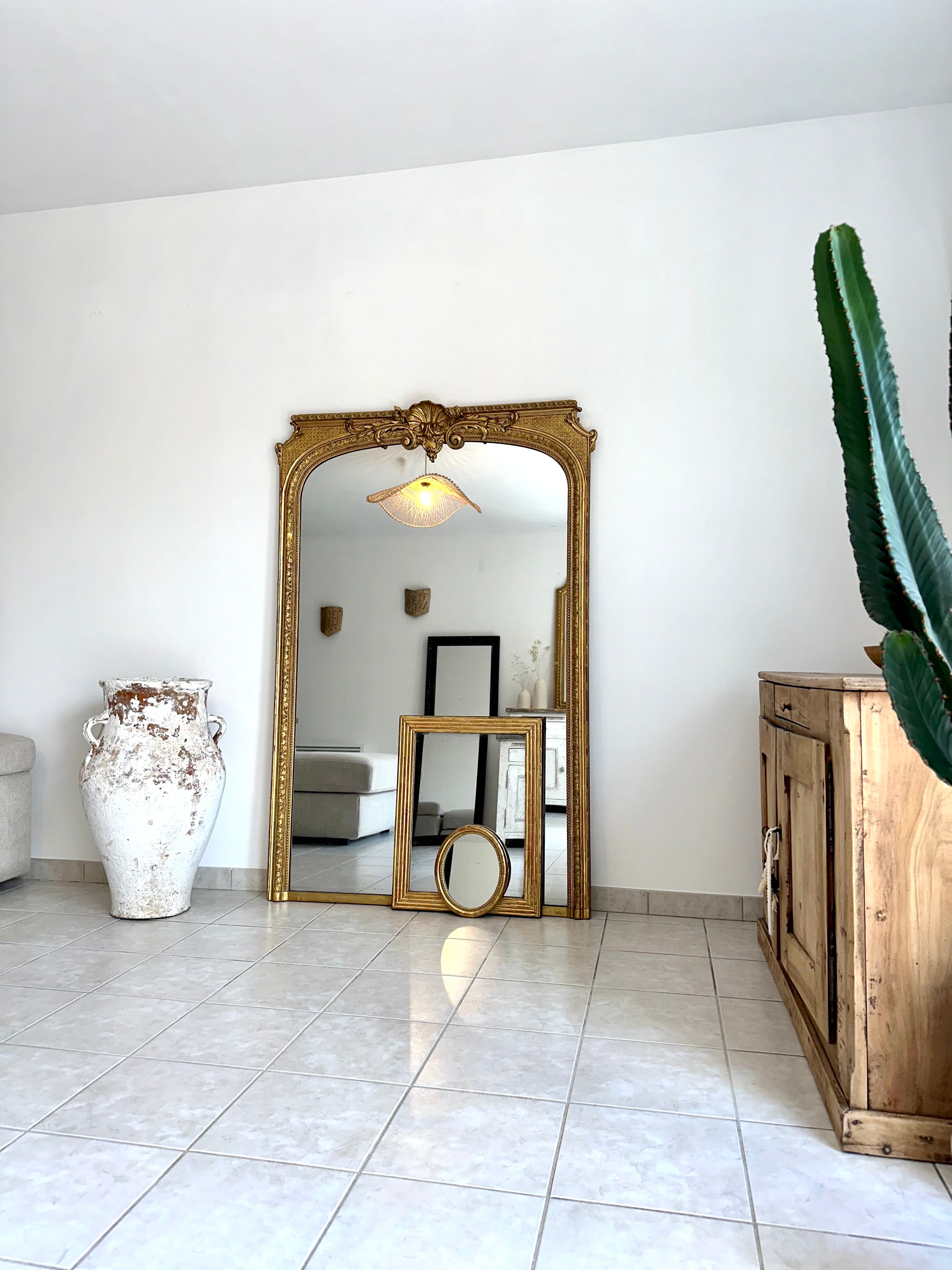 Grands et petits miroirs anciens dorés posés au sol dans le salon à coté d'une jarre